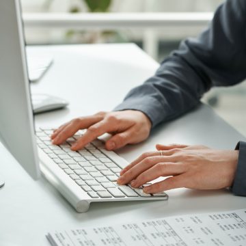 Close-up of female manager typing document on computer keyboard at her table at office